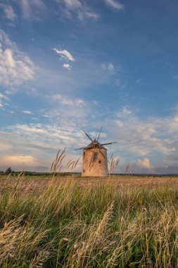 Manzarada ahşap kanatları olan yel değirmeni. Tarlalar, çayırlar ve çiçekler gün batımında belirir. Doğada bir değirmenle çekilmiş manzara. Macaristan 'daki Balaton bölgesi için tarihsel olarak alışılmadık bir durum.
