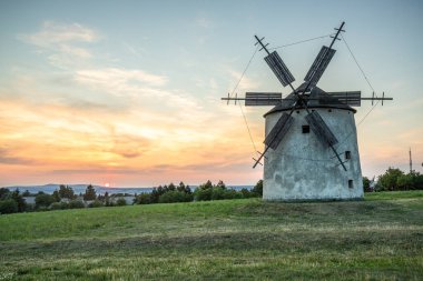 Windmill with wooden wings in a landscape setting. Fields, meadows and flowers appear in the sunset. Landscape shot in nature with a mill. historically untypical for the Balaton region in Hungary clipart