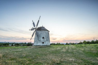 Manzarada ahşap kanatları olan yel değirmeni. Tarlalar, çayırlar ve çiçekler gün batımında belirir. Doğada bir değirmenle çekilmiş manzara. Macaristan 'daki Balaton bölgesi için tarihsel olarak alışılmadık bir durum.