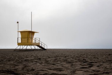 Deniz manzarası var. Siyah lav plajında sarı cankurtaran kulübeleri olan şehir plajı. Gran Tarajal, Las Palmas, Fuerteventura, İspanya 'da kumlu havuz