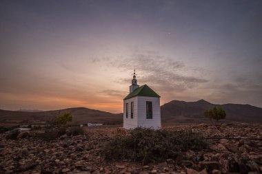 Verimsiz volkanik bir arazide küçük, beyaz ahşap bir şapel. Gündoğumu, İspanya 'nın Kanarya Adaları' ndaki Fuerteventura Adası 'ndaki Ermita Protestante de Violante kilisesinin manzara görüntüsü.