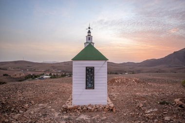 Verimsiz volkanik bir arazide küçük, beyaz ahşap bir şapel. Gündoğumu, İspanya 'nın Kanarya Adaları' ndaki Fuerteventura Adası 'ndaki Ermita Protestante de Violante kilisesinin manzara görüntüsü.