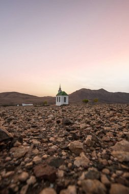 Verimsiz volkanik bir arazide küçük, beyaz ahşap bir şapel. Gündoğumu, İspanya 'nın Kanarya Adaları' ndaki Fuerteventura Adası 'ndaki Ermita Protestante de Violante kilisesinin manzara görüntüsü.