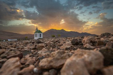 small cute white wooden chapel in a barren volcanic landscape. Sunset, landscape shot of the Ermita Protestante de Violante church, on the island of Fuerteventura, Canary Islands, Spain clipart