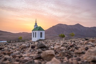 small cute white wooden chapel in a barren volcanic landscape. Sunset, landscape shot of the Ermita Protestante de Violante church, on the island of Fuerteventura, Canary Islands, Spain clipart