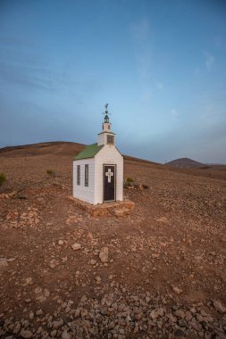 Verimsiz volkanik bir arazide küçük, beyaz ahşap bir şapel. Gündoğumu, İspanya 'nın Kanarya Adaları' ndaki Fuerteventura Adası 'ndaki Ermita Protestante de Violante kilisesinin manzara görüntüsü.