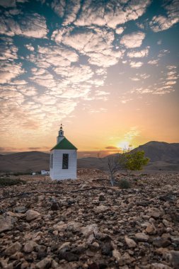 Verimsiz volkanik bir arazide küçük, beyaz ahşap bir şapel. Gündoğumu, İspanya 'nın Kanarya Adaları' ndaki Fuerteventura Adası 'ndaki Ermita Protestante de Violante kilisesinin manzara görüntüsü.