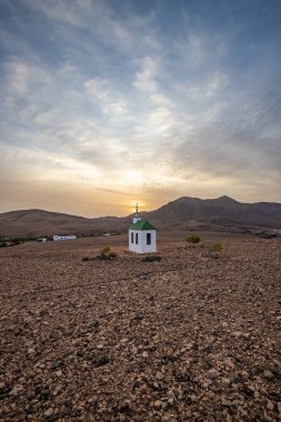 small cute white wooden chapel in a barren volcanic landscape. Sunset, landscape shot of the Ermita Protestante de Violante church, on the island of Fuerteventura, Canary Islands, Spain clipart