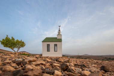 Verimsiz volkanik bir arazide küçük, beyaz ahşap bir şapel. Günbatımı, İspanya 'nın Kanarya Adaları' ndaki Fuerteventura Adası 'ndaki Ermita Protestante de Violante kilisesinin manzara görüntüsü.