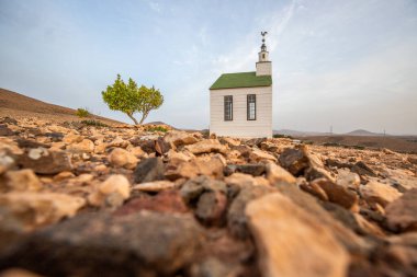 small cute white wooden chapel in a barren volcanic landscape. Sunrise, landscape shot of Ermita Protestante de Violante church, on Fuerteventura island, Canary Islands, Spain clipart