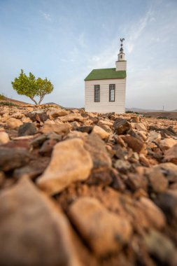 small cute white wooden chapel in a barren volcanic landscape. Sunset, landscape shot of the Ermita Protestante de Violante church, on the island of Fuerteventura, Canary Islands, Spain clipart