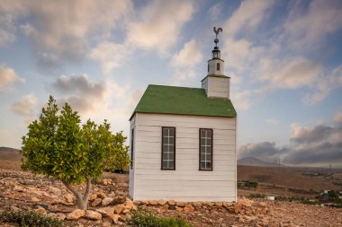 small cute white wooden chapel in a barren volcanic landscape. Sunrise, landscape shot of Ermita Protestante de Violante church, on Fuerteventura island, Canary Islands, Spain clipart