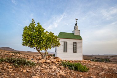 small cute white wooden chapel in a barren volcanic landscape. Sunrise, landscape shot of Ermita Protestante de Violante church, on Fuerteventura island, Canary Islands, Spain clipart