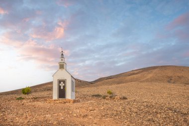 Verimsiz volkanik bir arazide küçük, beyaz ahşap bir şapel. Gündoğumu, İspanya 'nın Kanarya Adaları' ndaki Fuerteventura Adası 'ndaki Ermita Protestante de Violante kilisesinin manzara görüntüsü.