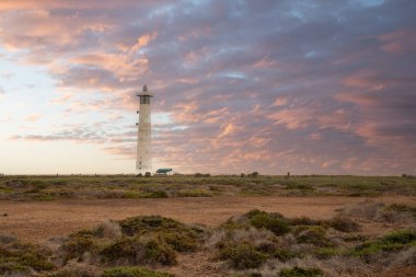Doğa koruma alanında deniz feneriyle çekilen alacakaranlık manzarası. Gün batımında deniz manzarası. Hafif bir Kalima sırasında deniz feneri, Morro Jable 'da kum fırtınası, Fuerteventura, Kanarya Adaları, İspanya