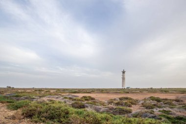 Doğa koruma alanında deniz feneriyle çekilen alacakaranlık manzarası. Gün batımında deniz manzarası. Hafif bir Kalima sırasında deniz feneri, Morro Jable 'da kum fırtınası, Fuerteventura, Kanarya Adaları, İspanya