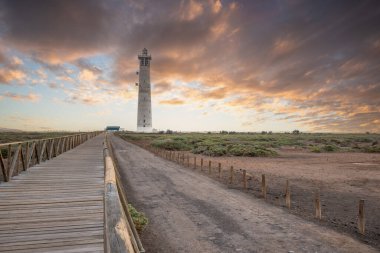 Doğa koruma alanında deniz feneriyle çekilen alacakaranlık manzarası. Gün batımında deniz manzarası. Hafif bir Kalima sırasında deniz feneri, Morro Jable 'da kum fırtınası, Fuerteventura, Kanarya Adaları, İspanya