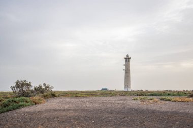 Doğa koruma alanında deniz feneriyle çekilen alacakaranlık manzarası. Gün batımında deniz manzarası. Hafif bir Kalima sırasında deniz feneri, Morro Jable 'da kum fırtınası, Fuerteventura, Kanarya Adaları, İspanya