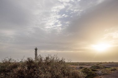 Doğa koruma alanında deniz feneriyle çekilen alacakaranlık manzarası. Gün batımında deniz manzarası. Hafif bir Kalima sırasında deniz feneri, Morro Jable 'da kum fırtınası, Fuerteventura, Kanarya Adaları, İspanya
