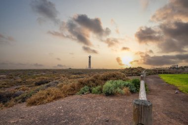 Doğa koruma alanında deniz feneriyle çekilen alacakaranlık manzarası. Gün batımında deniz manzarası. Hafif bir Kalima sırasında deniz feneri, Morro Jable 'da kum fırtınası, Fuerteventura, Kanarya Adaları, İspanya