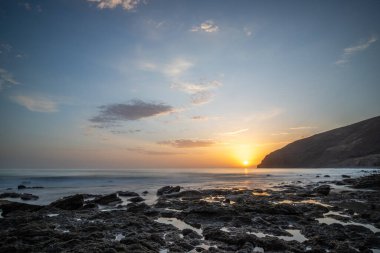 Körfezde gün batımı. Dalgaların çekildiği çorak bir kıyı manzarası olan güzel bir manzara. Hafif bir Calima ile, Gran Tarajal, Kanarya Adaları, Fuerteventura, İspanya 'da büyük gökyüzü renginde alacakaranlık