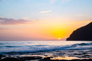 Körfezde gün batımı. Dalgaların çekildiği çorak bir kıyı manzarası olan güzel bir manzara. Hafif bir Calima ile, Gran Tarajal, Kanarya Adaları, Fuerteventura, İspanya 'da büyük gökyüzü renginde alacakaranlık