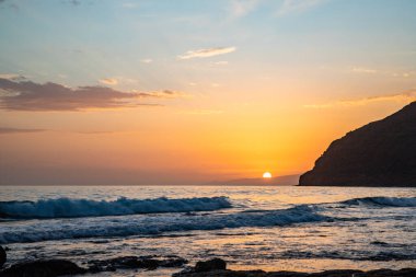 Körfezde gün batımı. Dalgaların çekildiği çorak bir kıyı manzarası olan güzel bir manzara. Hafif bir Calima ile, Gran Tarajal, Kanarya Adaları, Fuerteventura, İspanya 'da büyük gökyüzü renginde alacakaranlık