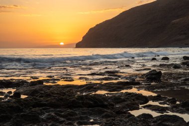 Körfezde gün batımı. Dalgaların çekildiği çorak bir kıyı manzarası olan güzel bir manzara. Hafif bir Calima ile, Gran Tarajal, Kanarya Adaları, Fuerteventura, İspanya 'da büyük gökyüzü renginde alacakaranlık