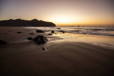 Sabah kumsalda. Güneşin doğuşunda deniz manzarası. Koyun kıyı şeridi, hafif bir kum fırtınası sırasında siyah kumlar, bir Calima. Gran Tarajal, Kanarya Adaları, İspanya
