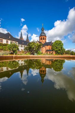 A historic monastery in the morning. Monastery walls, church and buildings are reflected in the water of a fountain. Beautiful garden in Seligenstadt Monastery, Germany clipart