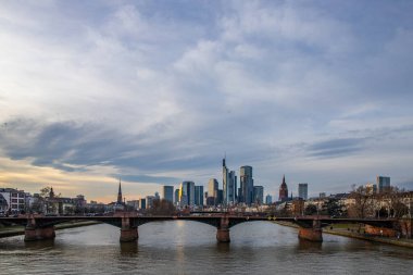 Gün batımında büyük bir şehir. Nehrin ufuk çizgisi üzerinde modern binalar. Yüksek binalar suya yansıtılır. Frankfurt am Main, Almanya 'nın modern mimarisi