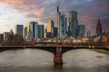 Gün batımında büyük bir şehir. Nehrin ufuk çizgisi üzerinde modern binalar. Yüksek binalar suya yansıtılır. Frankfurt am Main, Almanya 'nın modern mimarisi