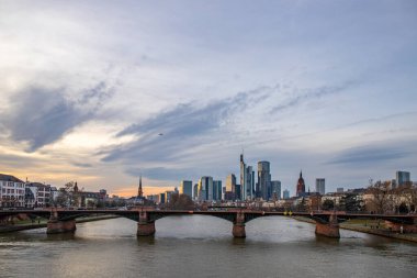 Gün batımında büyük bir şehir. Nehrin ufuk çizgisi üzerinde modern binalar. Yüksek binalar suya yansıtılır. Frankfurt am Main, Almanya 'nın modern mimarisi