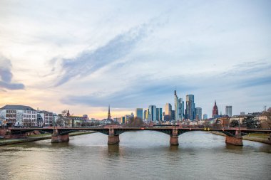 Gün batımında büyük bir şehir. Nehrin ufuk çizgisi üzerinde modern binalar. Yüksek binalar suya yansıtılır. Frankfurt am Main, Almanya 'nın modern mimarisi