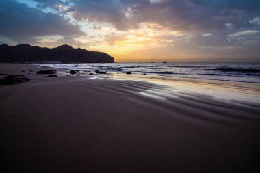 Sabah kumsalda. Güneşin doğuşunda deniz manzarası. Koyun kıyı şeridi, hafif bir kum fırtınası sırasında siyah kumlar, bir Calima. Gran Tarajal, Kanarya Adaları, İspanya