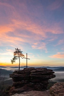 Doğanın sabahki manzarası. Vadide sis ve kumtaşı uçurumunda bir zirve haçı. Almanya 'nın Derebeyi Ormanı' nda Gün Doğumu