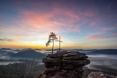 Doğanın sabahki manzarası. Vadide sis ve kumtaşı uçurumunda bir zirve haçı. Almanya 'nın Derebeyi Ormanı' nda Gün Doğumu