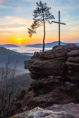 Doğanın sabahki manzarası. Vadide sis ve kumtaşı uçurumunda bir zirve haçı. Almanya 'nın Derebeyi Ormanı' nda Gün Doğumu