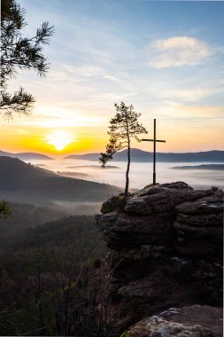 Doğanın sabahki manzarası. Vadide sis ve kumtaşı uçurumunda bir zirve haçı. Almanya 'nın Derebeyi Ormanı' nda Gün Doğumu