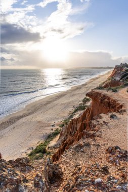 Atlantik Okyanusu 'nda çarpıcı oluşumları olan kayalıklar. Manzara çekiminde sıcak gün batımı. Sahilde ve denizde çarpıcı oluşumlara sahip kızıl kayalıklar, Praia da Falsia, Algarve, Portekiz