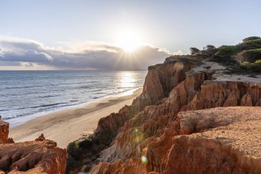 Atlantik Okyanusu 'nda çarpıcı oluşumları olan kayalıklar. Manzara çekiminde sıcak gün batımı. Sahilde ve denizde çarpıcı oluşumlara sahip kızıl kayalıklar, Praia da Falsia, Algarve, Portekiz
