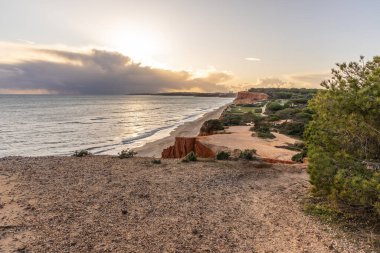 Atlantik Okyanusu 'nda çarpıcı oluşumları olan kayalıklar. Manzara çekiminde sıcak gün batımı. Sahilde ve denizde çarpıcı oluşumlara sahip kızıl kayalıklar, Praia da Falsia, Algarve, Portekiz