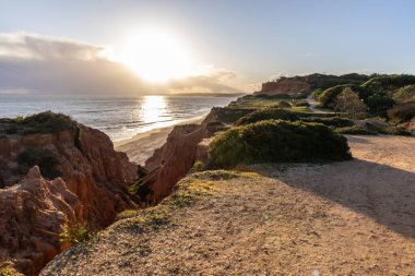 Atlantik Okyanusu 'nda çarpıcı oluşumları olan kayalıklar. Manzara çekiminde sıcak gün batımı. Sahilde ve denizde çarpıcı oluşumlara sahip kızıl kayalıklar, Praia da Falsia, Algarve, Portekiz