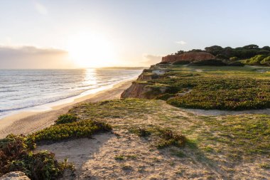 Atlantik Okyanusu 'nda çarpıcı oluşumları olan kayalıklar. Manzara çekiminde sıcak gün batımı. Sahilde ve denizde çarpıcı oluşumlara sahip kızıl kayalıklar, Praia da Falsia, Algarve, Portekiz
