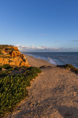 Atlantik Okyanusu 'nda çarpıcı oluşumları olan kayalıklar. Manzara çekiminde sıcak gün batımı. Sahilde ve denizde çarpıcı oluşumlara sahip kızıl kayalıklar, Praia da Falsia, Algarve, Portekiz