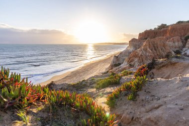 Atlantik Okyanusu 'nda çarpıcı oluşumları olan kayalıklar. Manzara çekiminde sıcak gün batımı. Sahilde ve denizde çarpıcı oluşumlara sahip kızıl kayalıklar, Praia da Falsia, Algarve, Portekiz