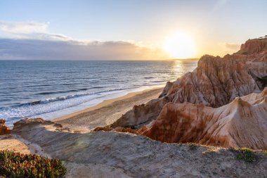 Atlantik Okyanusu 'nda çarpıcı oluşumları olan kayalıklar. Manzara çekiminde sıcak gün batımı. Sahilde ve denizde çarpıcı oluşumlara sahip kızıl kayalıklar, Praia da Falsia, Algarve, Portekiz