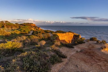 Atlantik Okyanusu 'nda çarpıcı oluşumları olan kayalıklar. Manzara çekiminde sıcak gün batımı. Sahilde ve denizde çarpıcı oluşumlara sahip kızıl kayalıklar, Praia da Falsia, Algarve, Portekiz