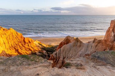 Atlantik Okyanusu 'nda çarpıcı oluşumları olan kayalıklar. Manzara çekiminde sıcak gün batımı. Sahilde ve denizde çarpıcı oluşumlara sahip kızıl kayalıklar, Praia da Falsia, Algarve, Portekiz