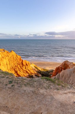 Atlantik Okyanusu 'nda çarpıcı oluşumları olan kayalıklar. Manzara çekiminde sıcak gün batımı. Sahilde ve denizde çarpıcı oluşumlara sahip kızıl kayalıklar, Praia da Falsia, Algarve, Portekiz